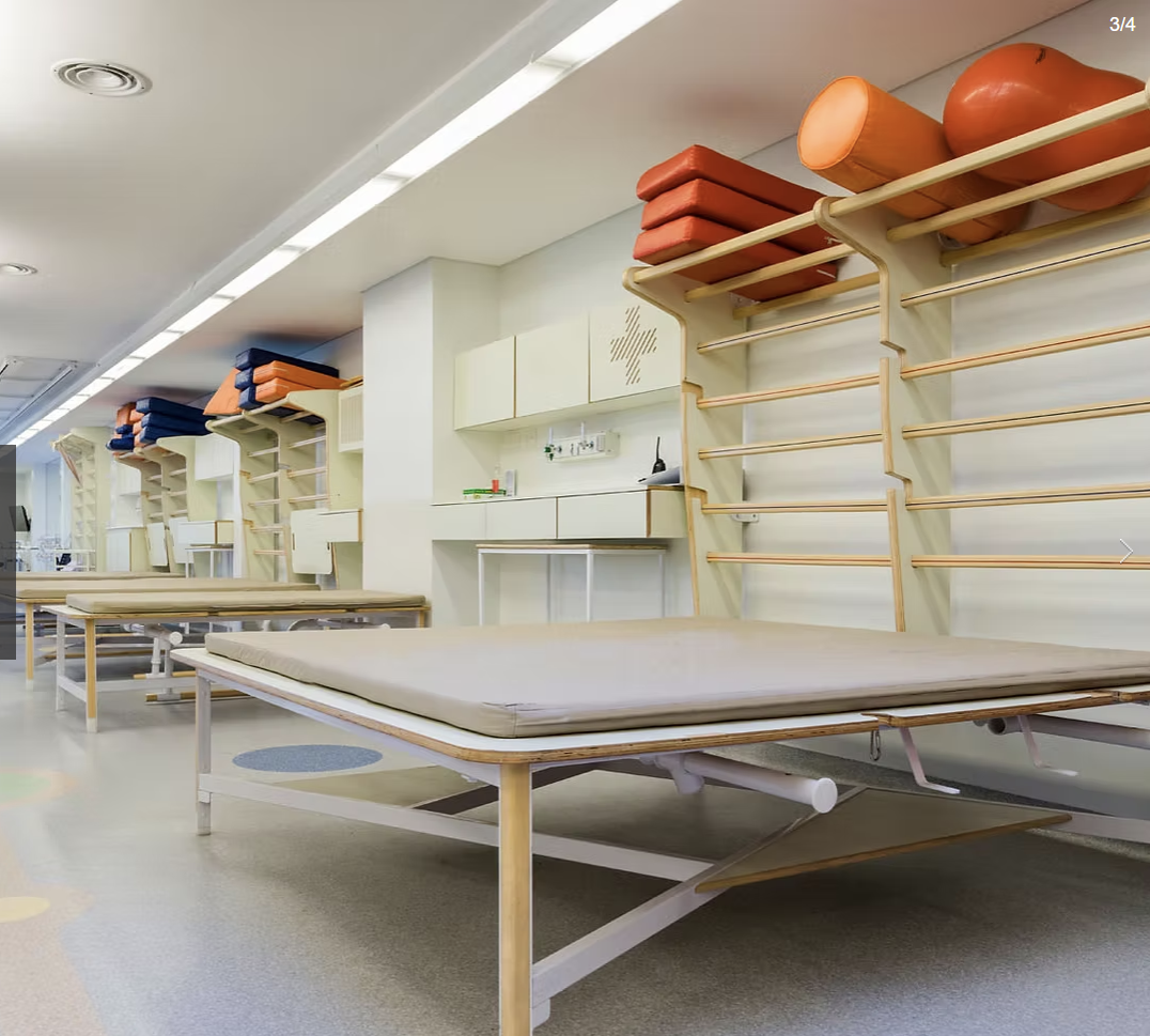 Multi-table treatment room with organised wall shelving and colour-coded rehabilitation equipment